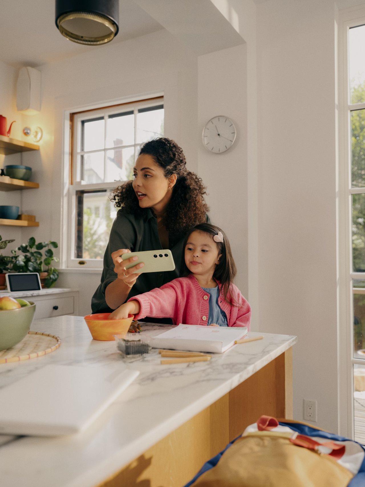 Mom in kitchen with little girl using cell phone.