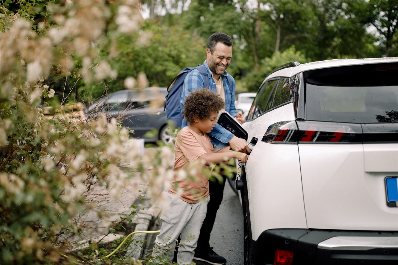 Dad and son plugging in SUV while parked on s side street.