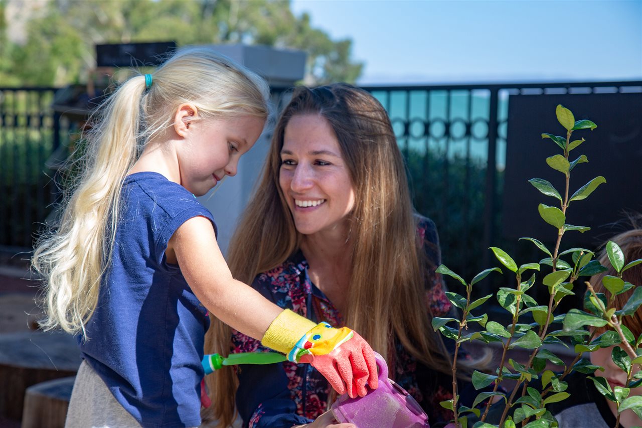 Woman and little girl watering flowers. Bright Horizons allows children to explore and learn through trial and error.