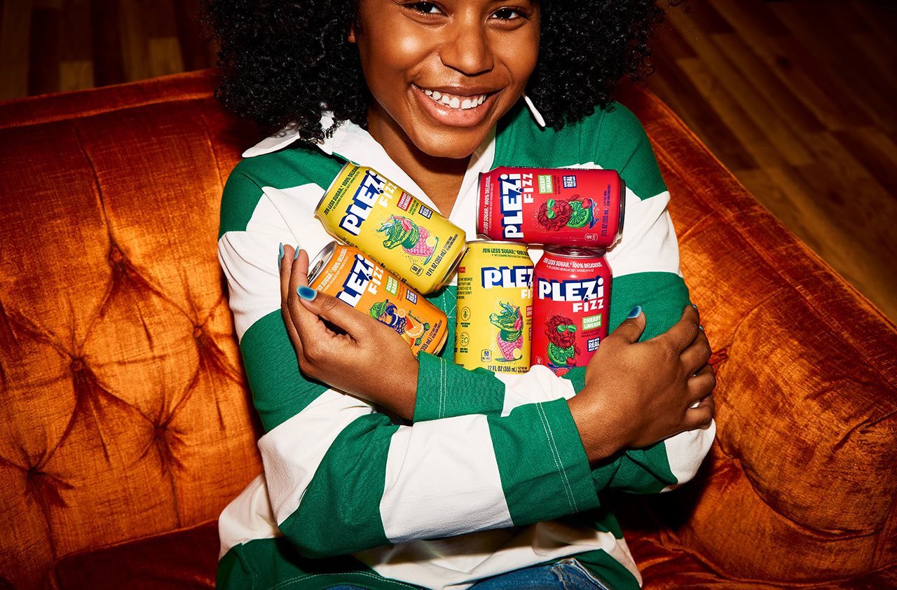Smiling girl sitting on a couch holding 5 cans of PLEZi close to her.