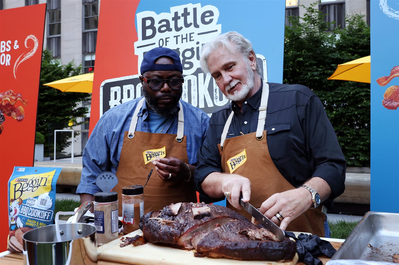 Two men in aprons grilling a pork shoulder on a grill outside