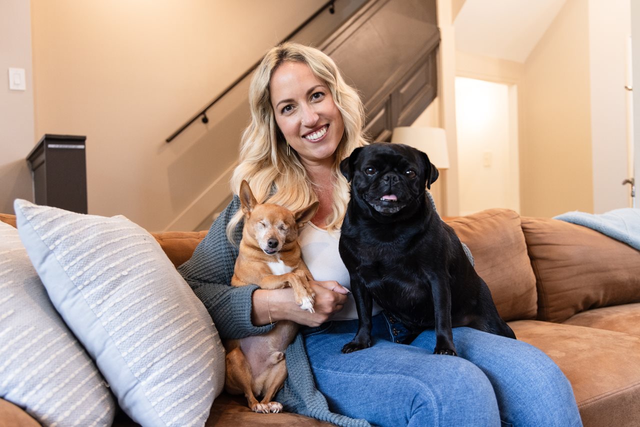 Smiling blond woman sitting on her couch with her two dogs.