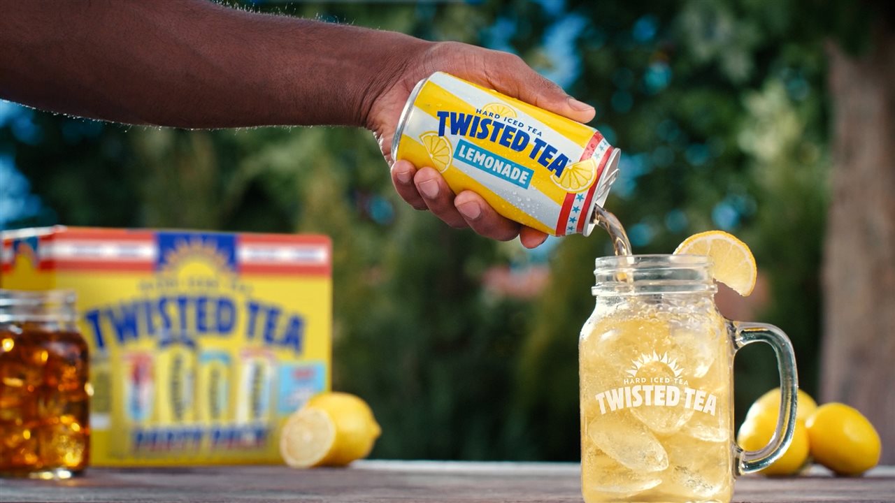 Close-up of person pouring a can of Twisted Tea Lemonade into a mug with ice and lemon.