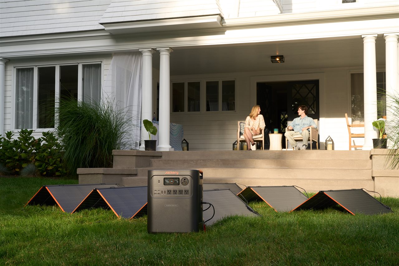 Couple sitting on backyard porch with the Jackery HomePower 3600 plus set up on the lawn.