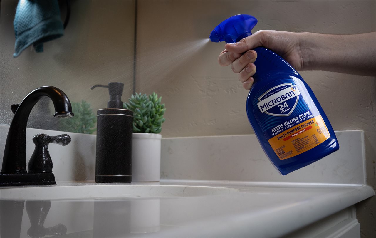 Person spraying the faucet handles in a bathroom with