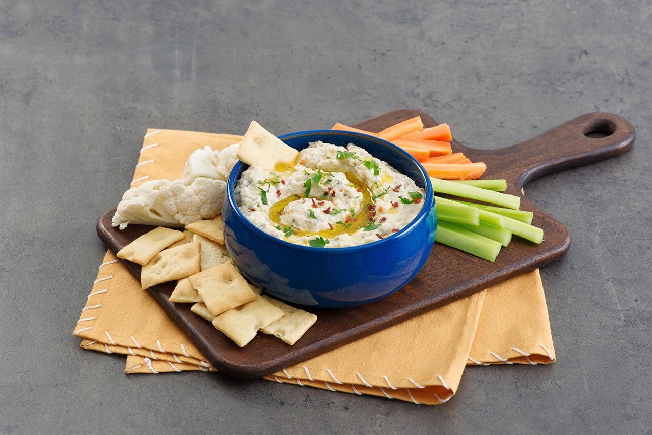 Charred Eggplant Yogurt Dip in a blue bowl surrounded by carrots and celery sticks and crackers.