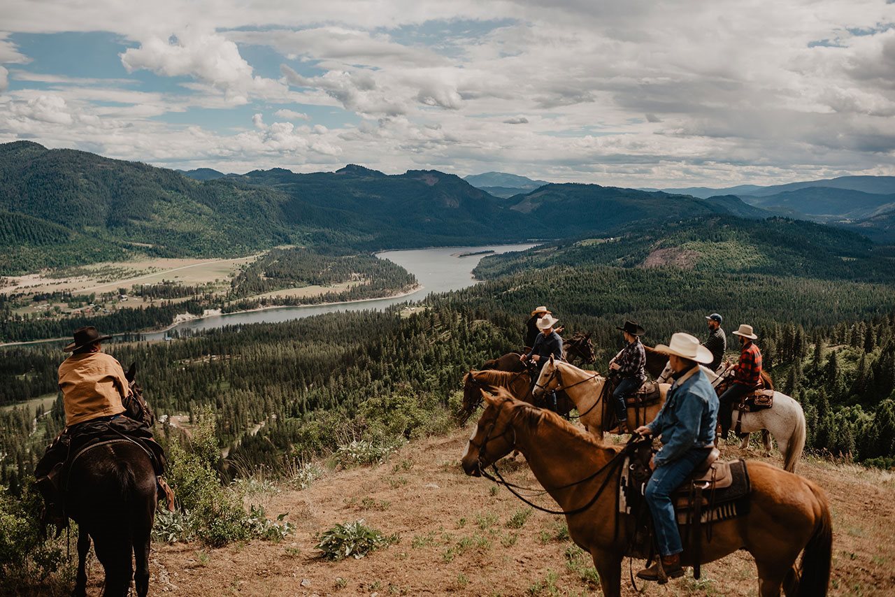 Seven men riding horses through a beautiful vista over looking a river on the Bull Hill Ranch.