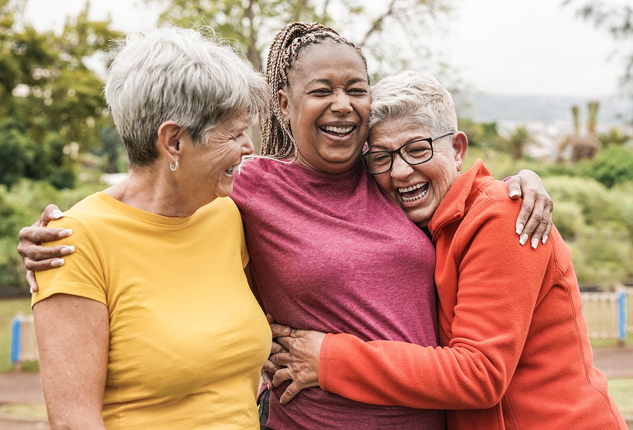 Three senior girl friends hugging and laughing while on a walk outdoors.
