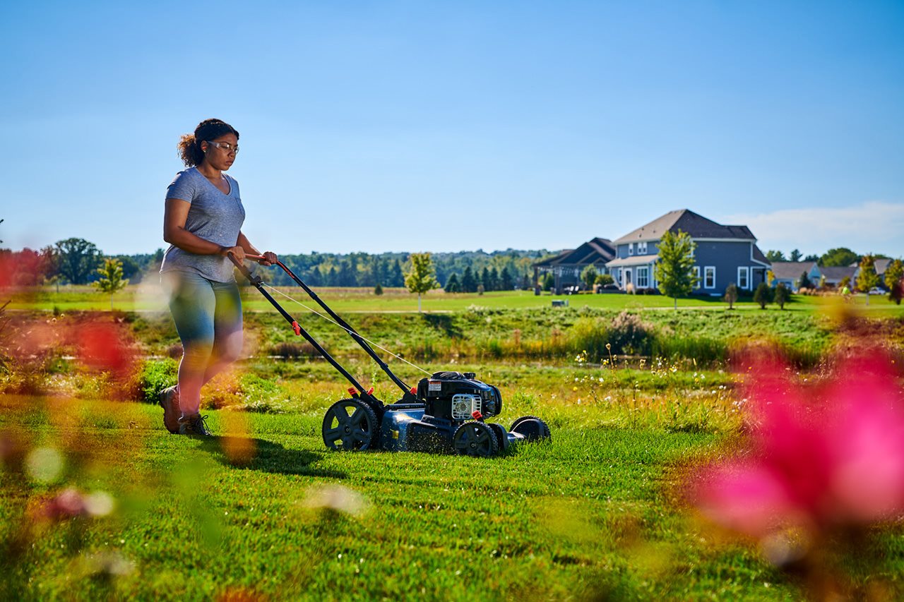 Woman pushing a gas powered lawn mower in the backyard.