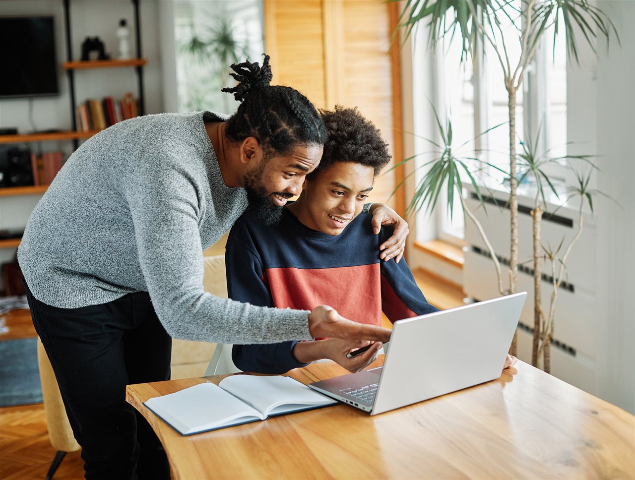 Father and son on laptop in livingroom learning about Pearson's Connections Academy AI policy for responsible AI use to help his child become a confident, adaptable, lifelong learner.
