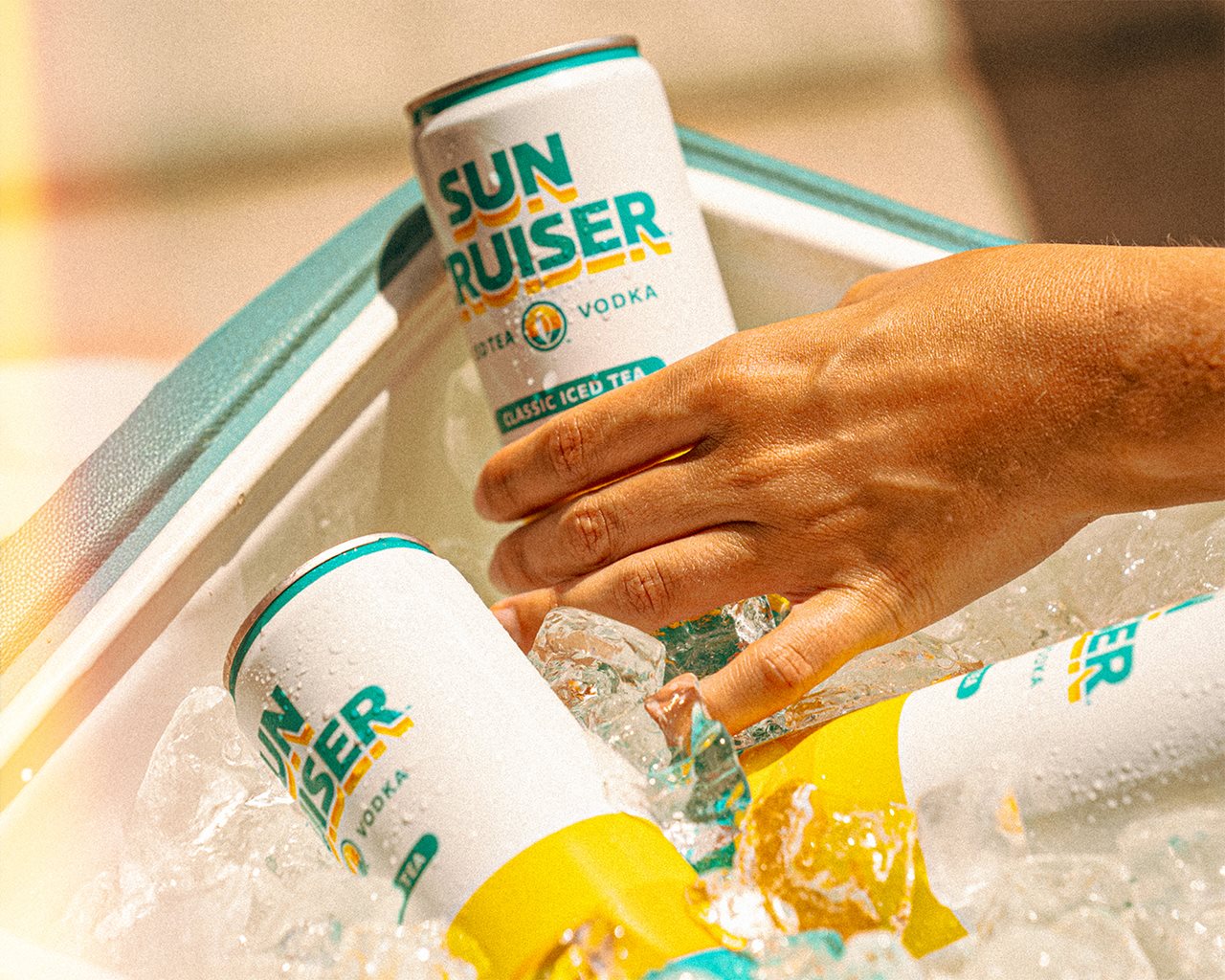 Hand reaching into a cooler for a can of Sun Cruiser IceTea Vodka.