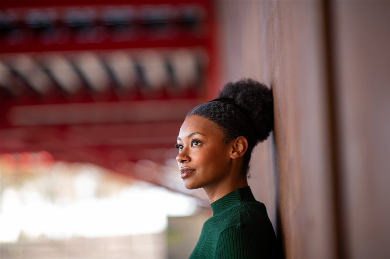 Woman leaning against a wall and looking upward.
