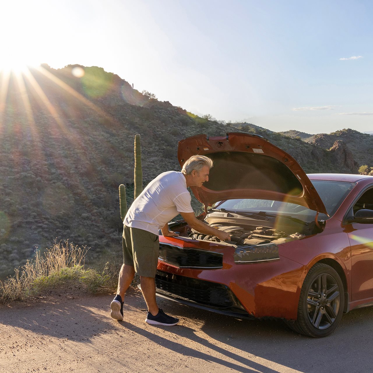 Man in the dessert with the hood popped on his car.