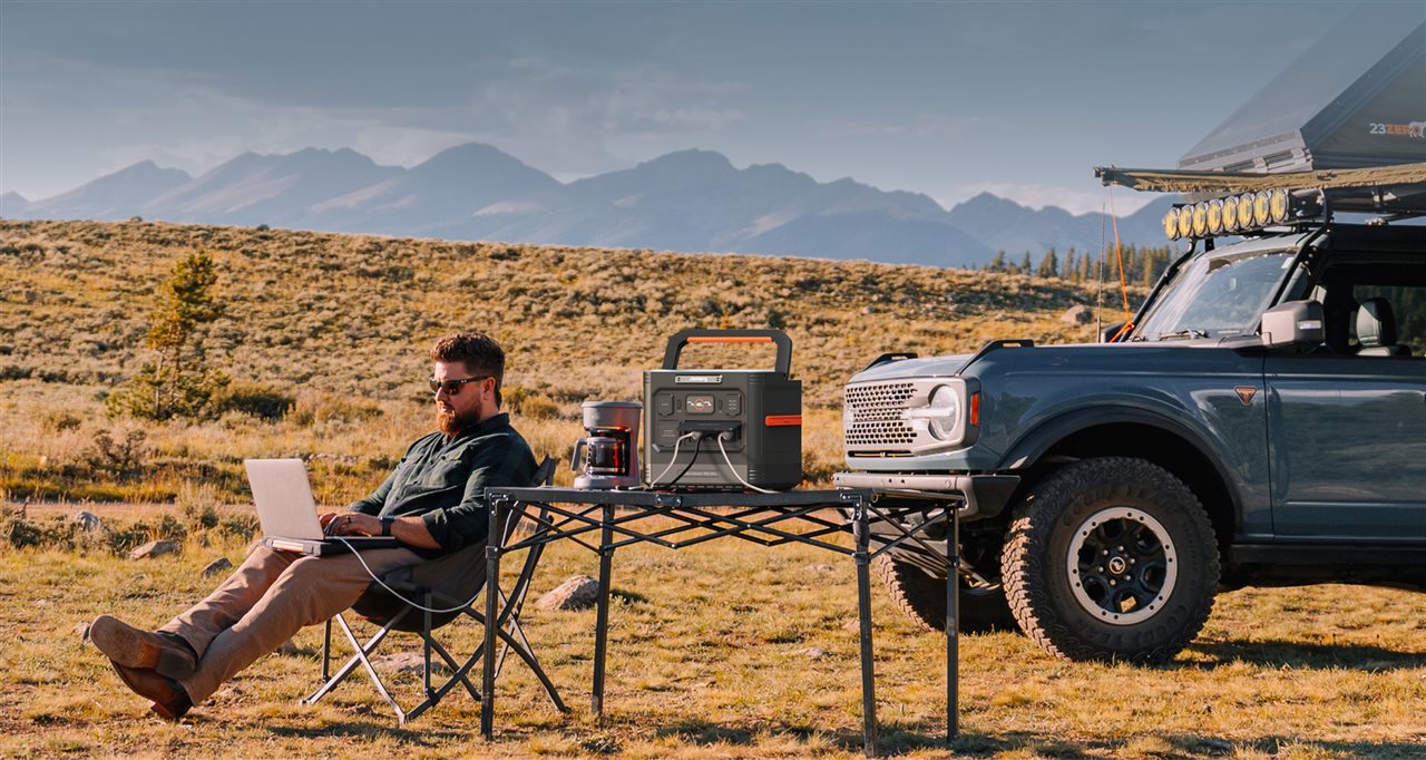 Man working on a computer and making a fresh pot of coffee powered by Jackery while enjoying the remote mountain vista.