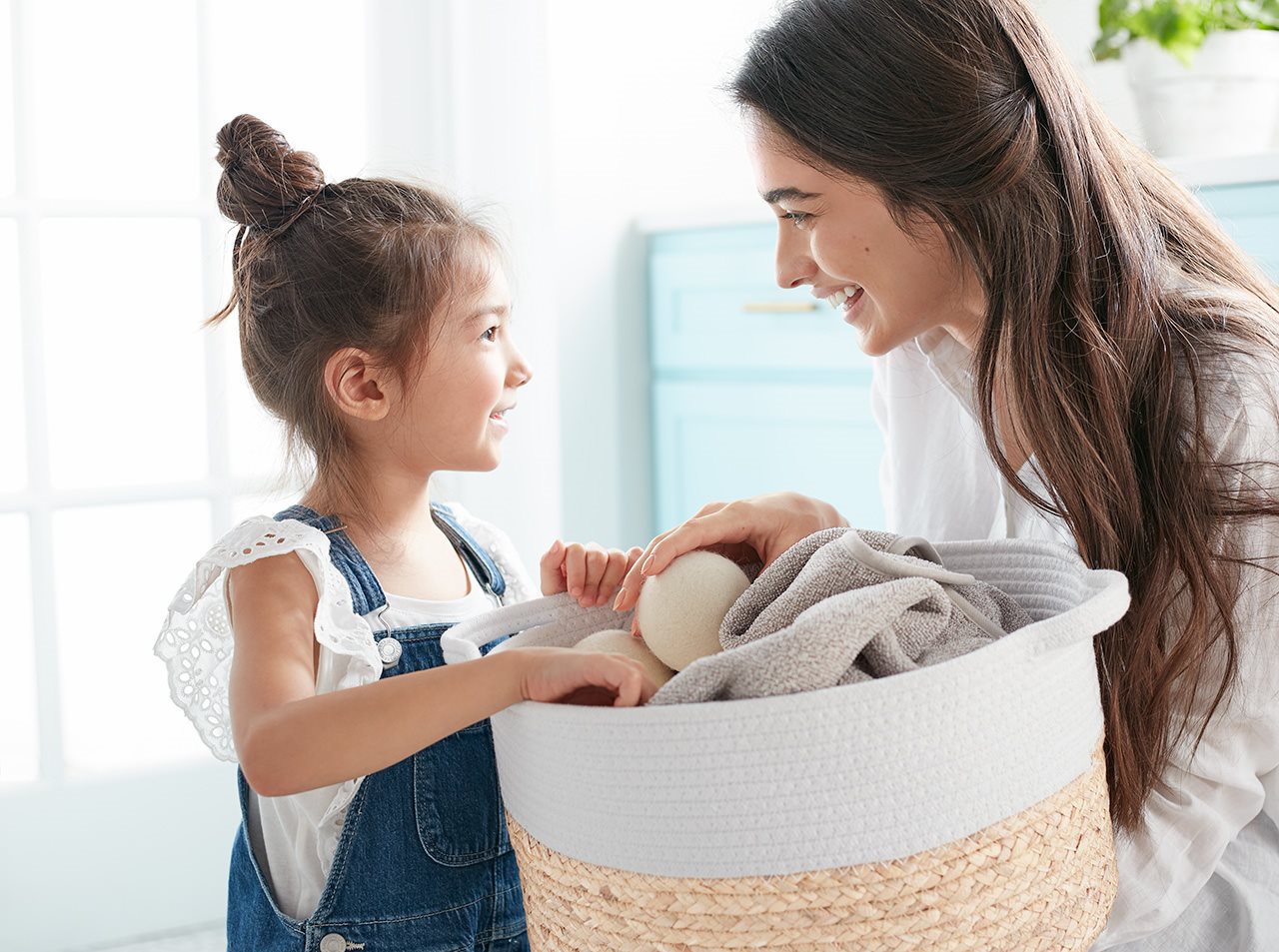 A woman and her daughter smile at each other as they both hold a basket of laundry.