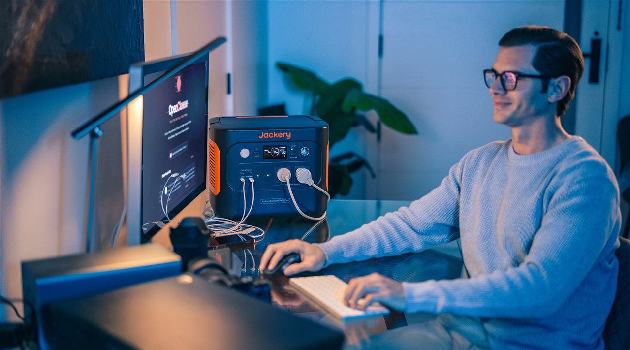 Man at home using desktop computer while it is plugged in to a Jackery back-up device.