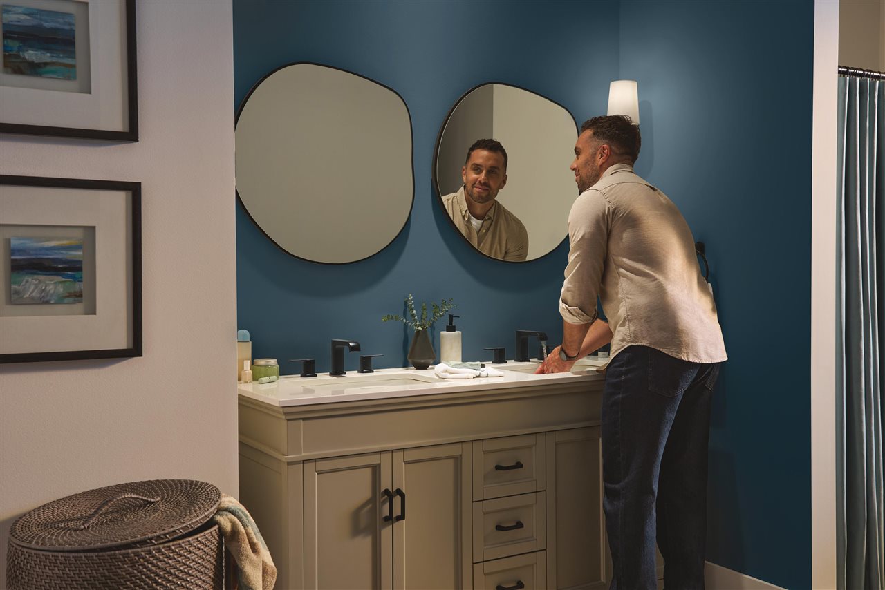 Man washing this hands in the bathroom sink and looking in the mirror.