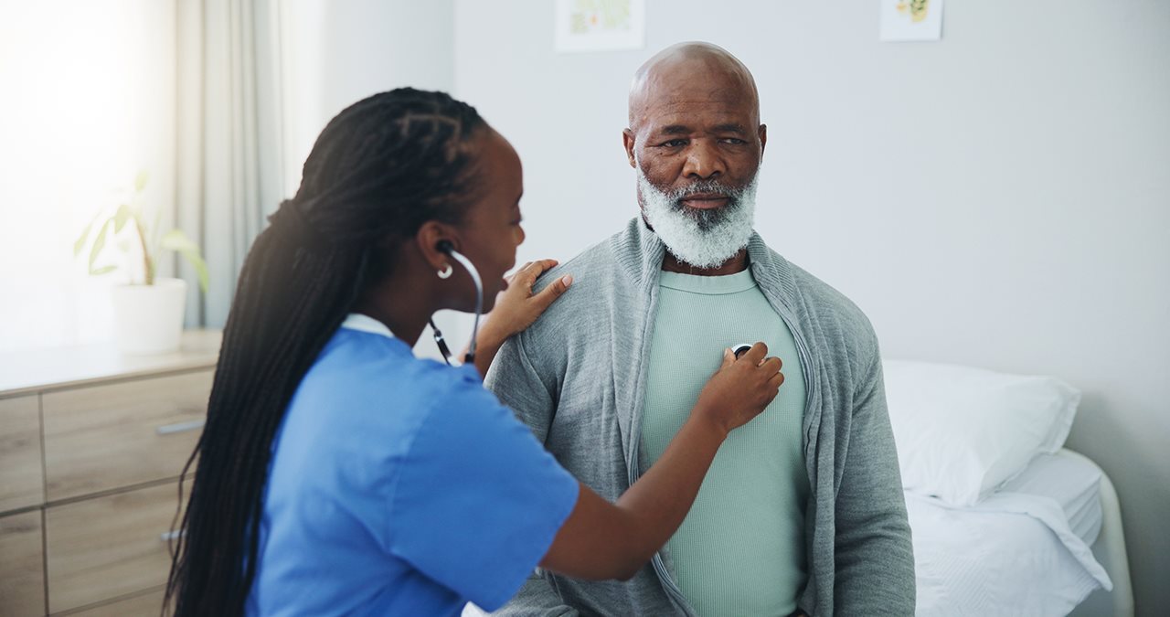 Woman doctor listening to older male patient heart using a stethoscope.
