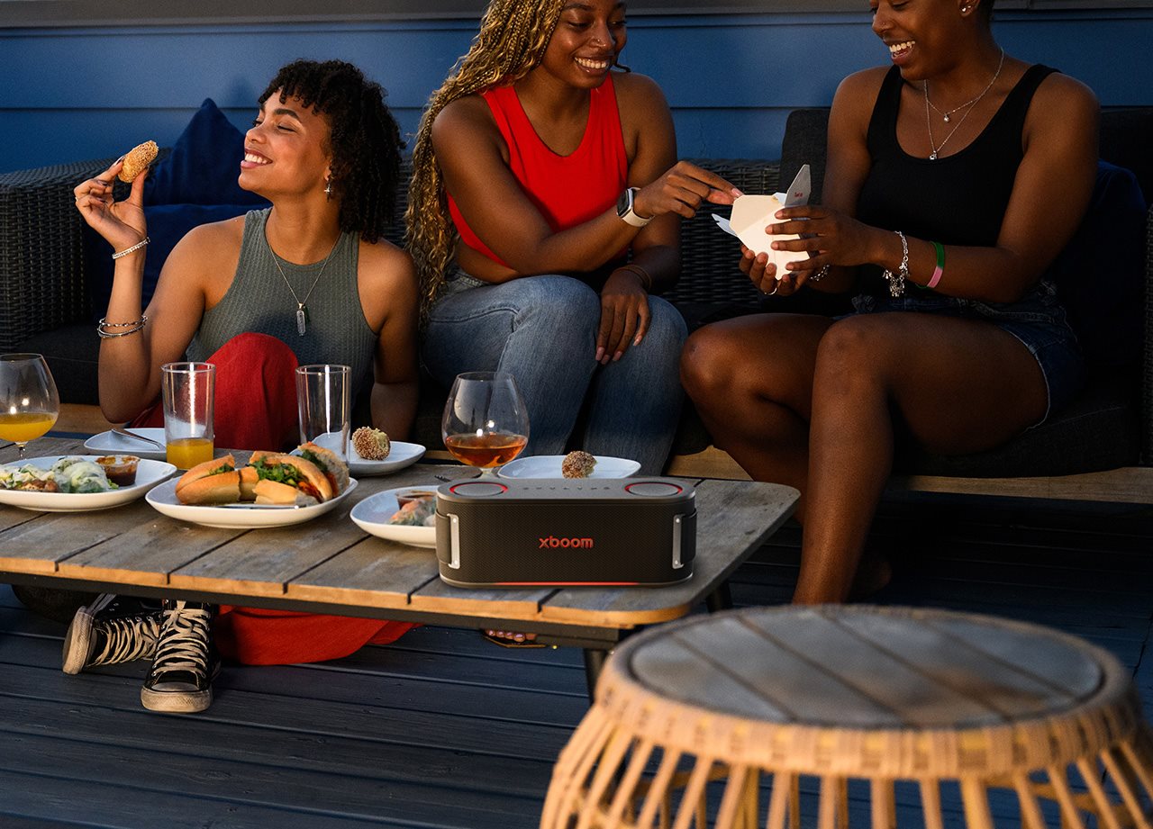 Friends eat dinner around a coffee table with an xboom speaker sitting on it.