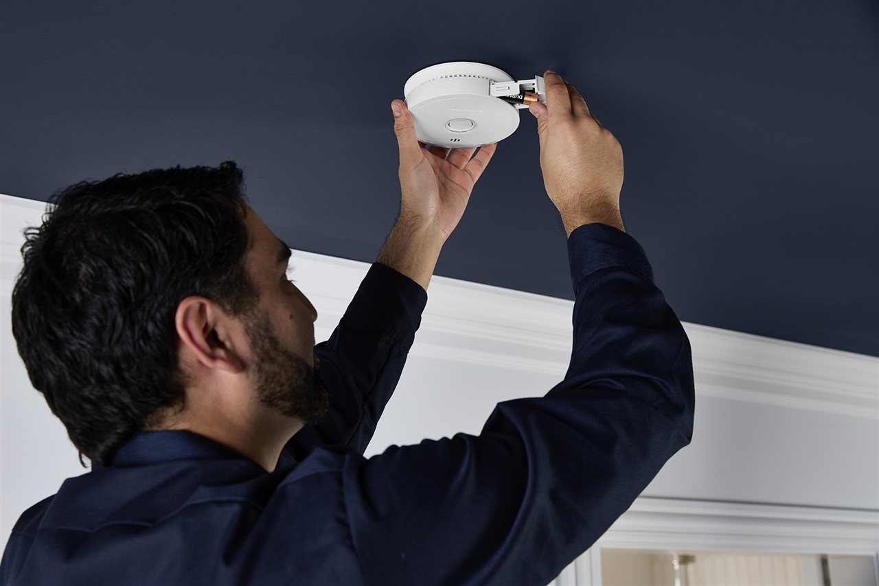 Man replacing the batteries in a First Alert smoke, CO and combination alarm which features a side-load battery drawer.