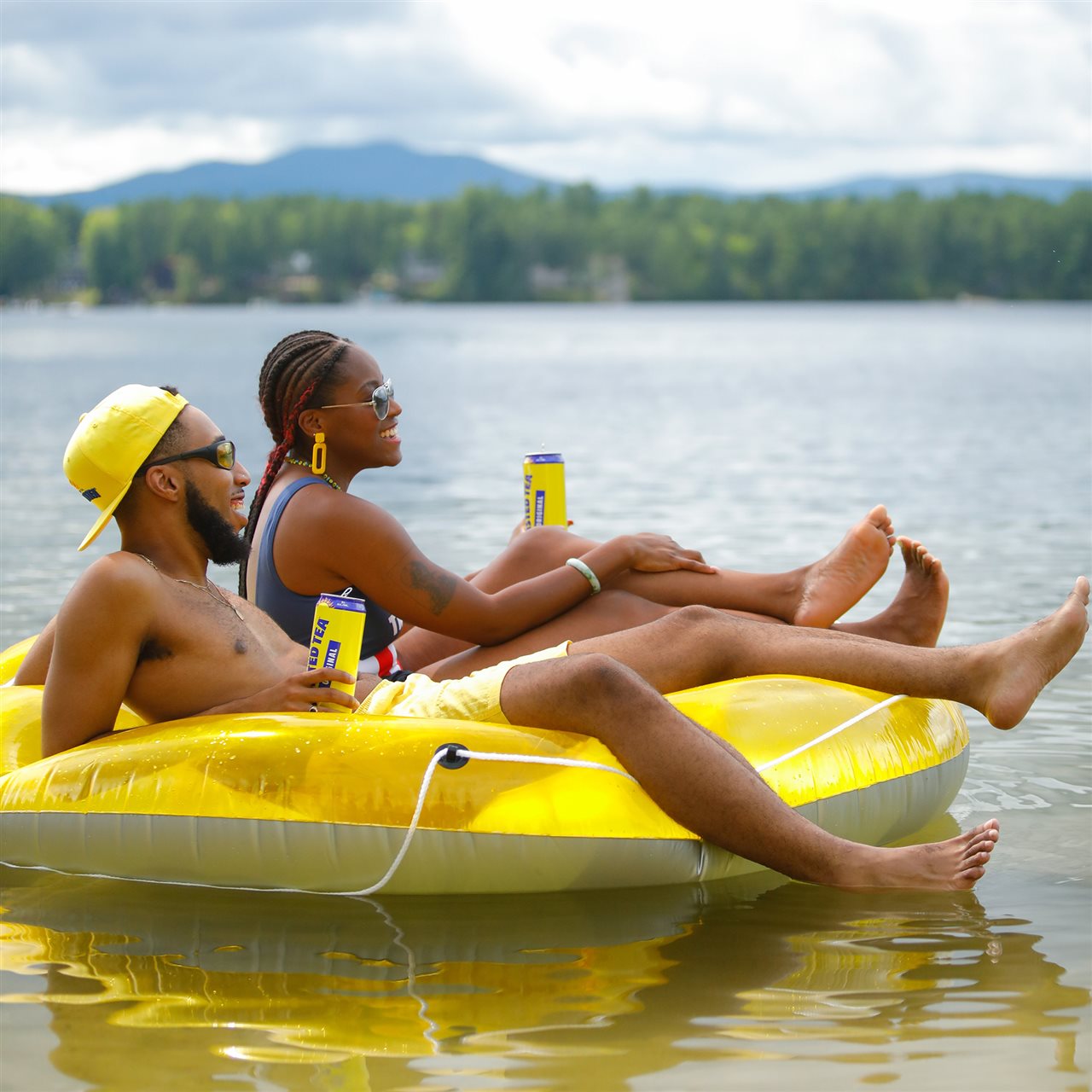 Two friends holding cans of Twisted Tea lemondade while sitting in an inflatable, floating on a lake.