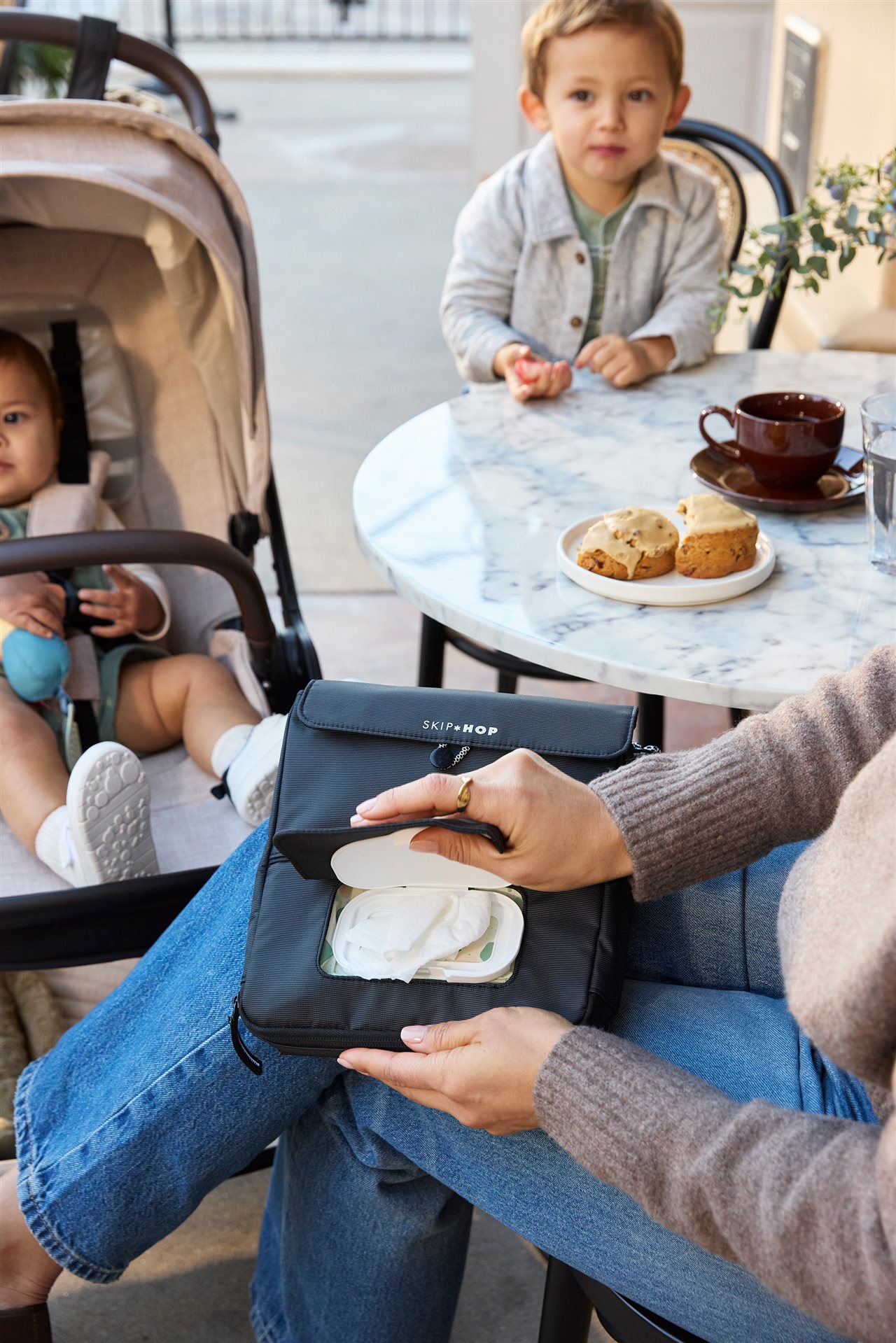 Mom opening a Carter's Skip Hop at and outdoor cafe with her two small children.