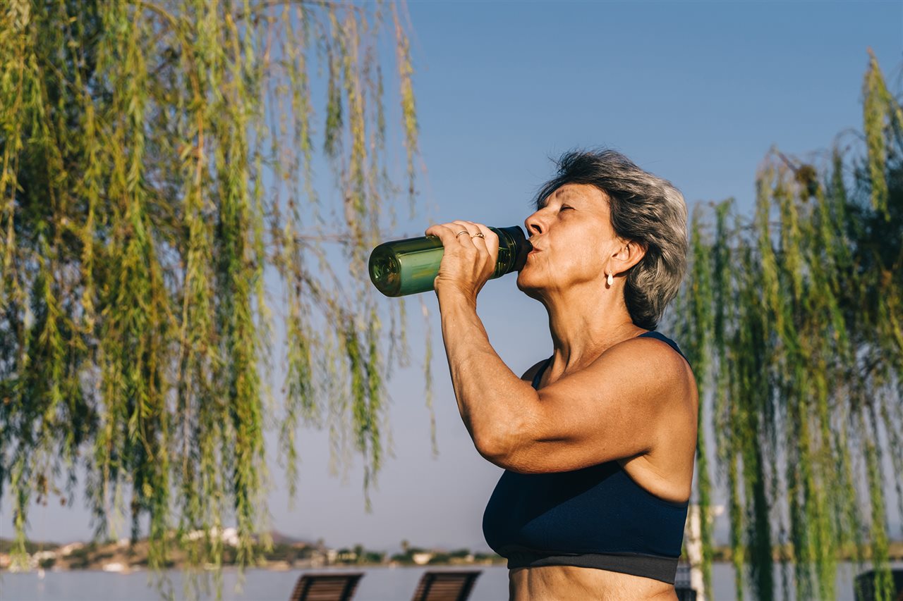 Mature woman drinking water while on a walk. Healthcare company, Abbott, recently conducted research on chronic disease.