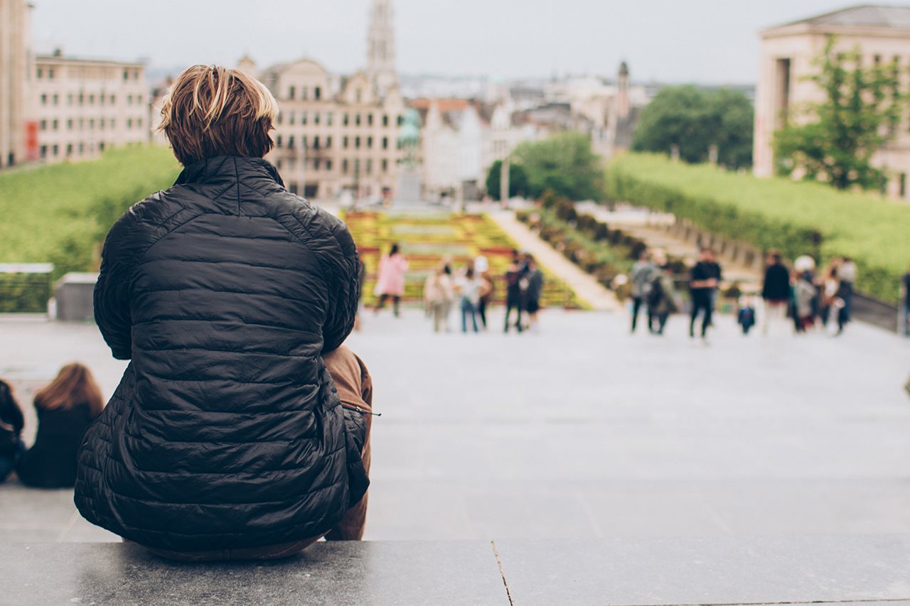 A woman with short hair in a black jacket sits on the top steps of a college campus.
