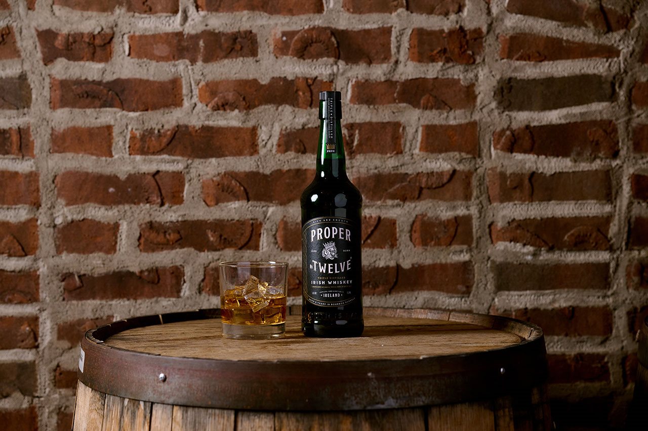 A bottle of Proper Twelve Irish Whiskey on a table next to a cocktail glass