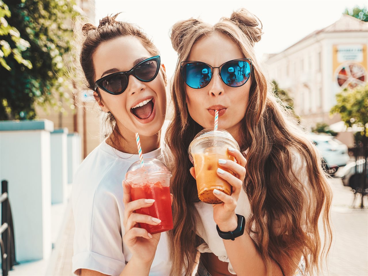 Two young women drinking soft drinks from cups with straws.