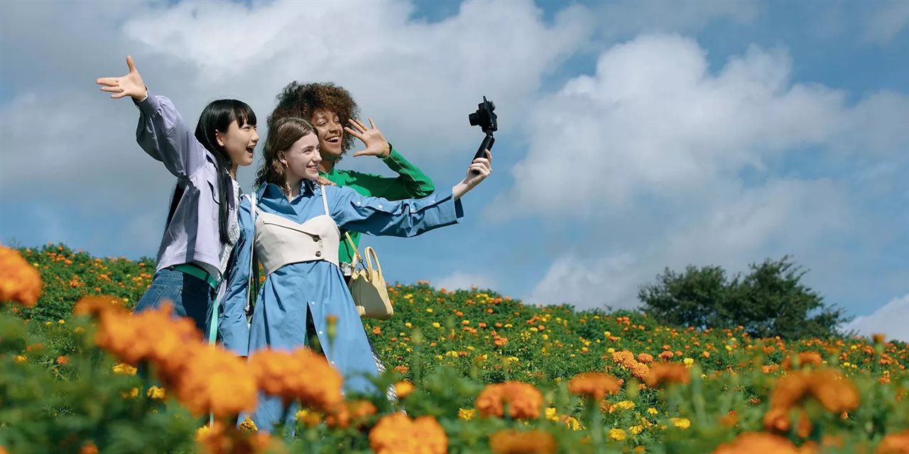 Group of three friends in a field of flowers taking a selfie with a Canon camera.