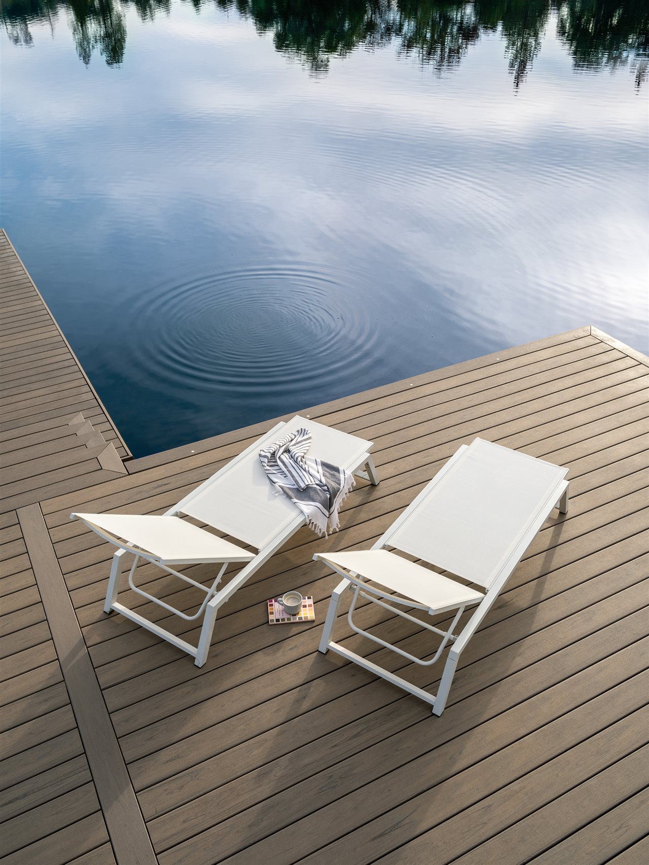 Two chairs on a wooden deck next to blue water.