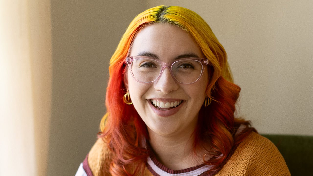Sonriente Alejandra con lentes y un suéter colorido mientras estaba sentada en el sofá.