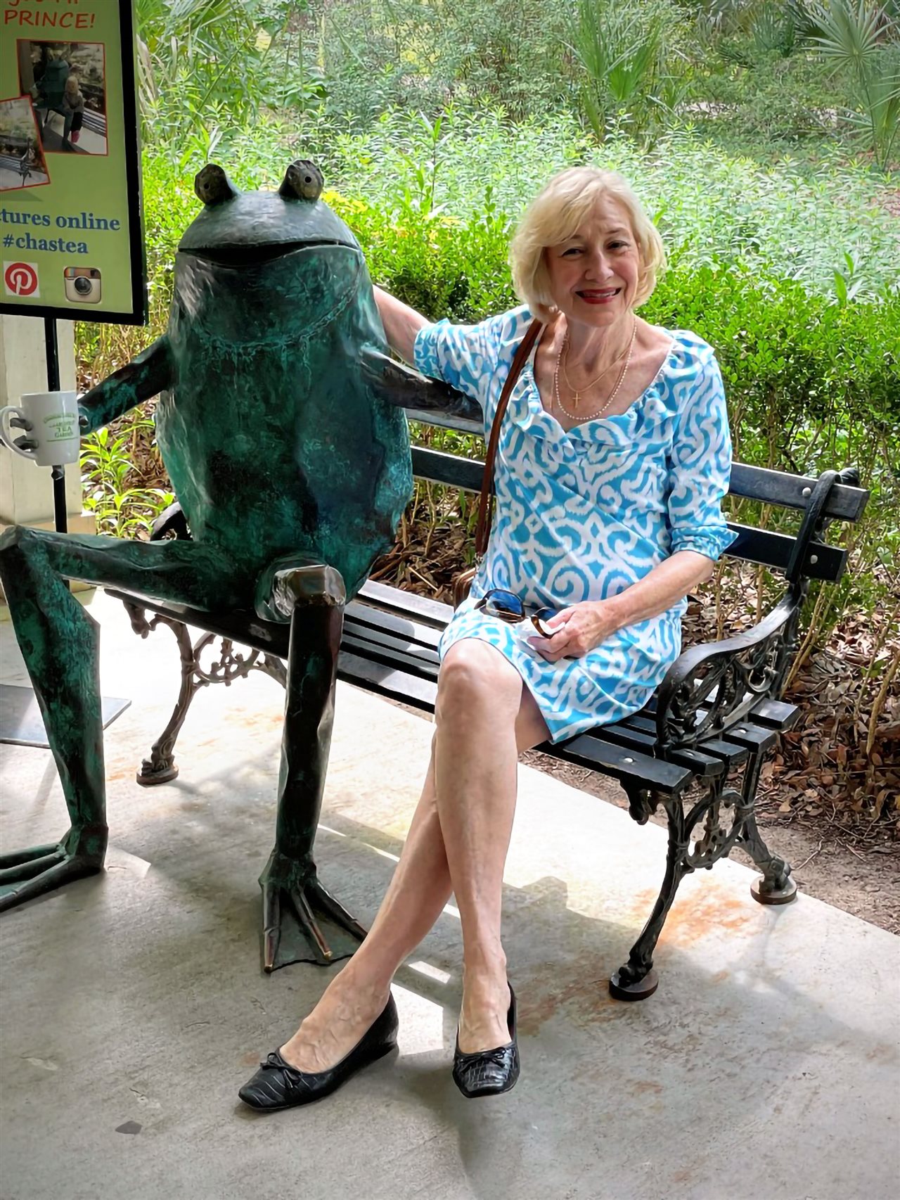 Smiling Lavonda sitting on a park bench with a statue of a frog.