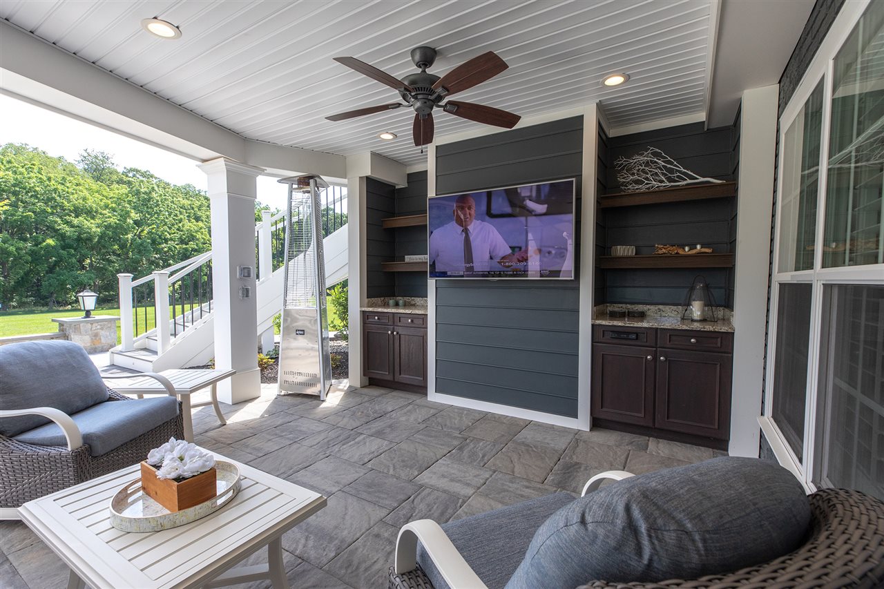 A weather-proof patio is decorated with an outdoor heater, furniture, a ceiling fan and a television.