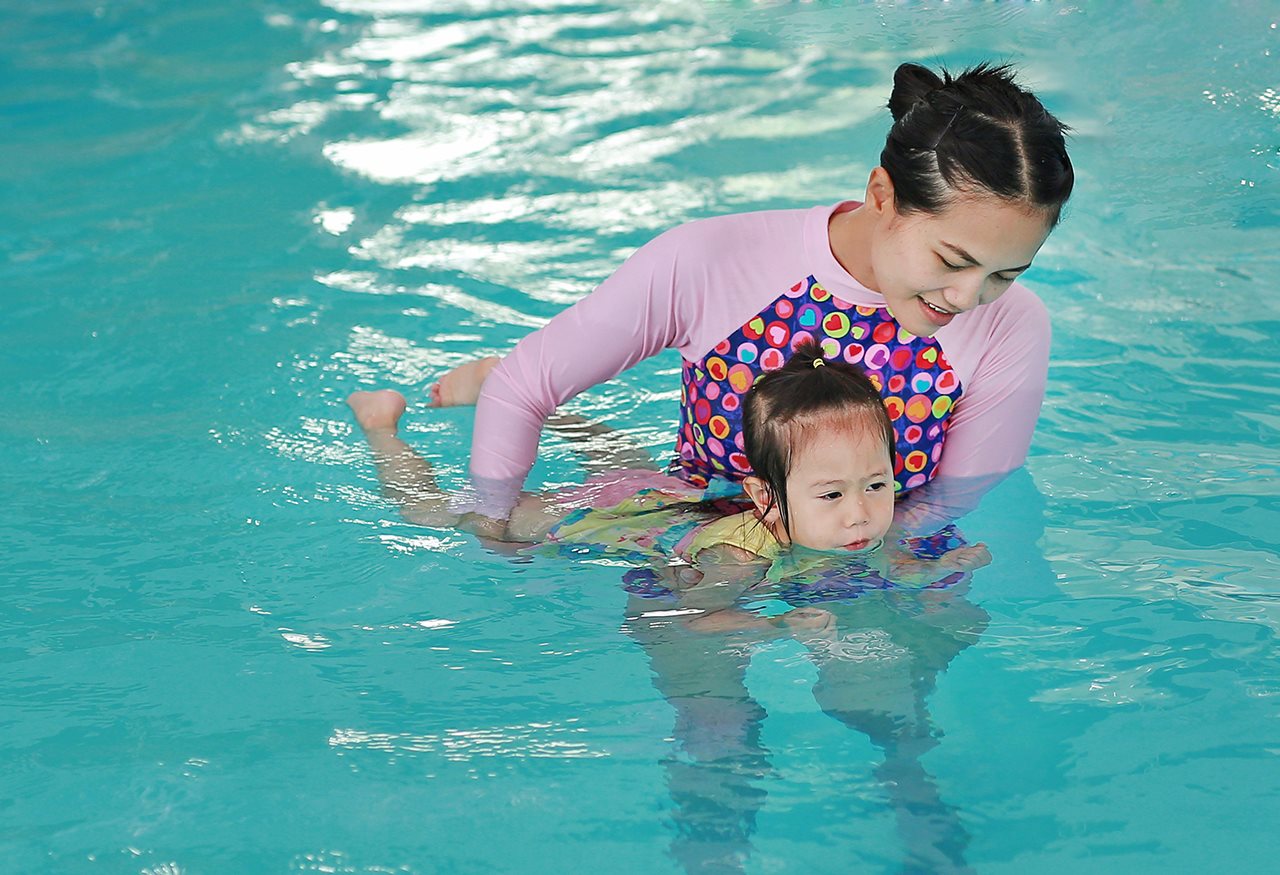 Mother, teaching little girl how to swim in a pool.