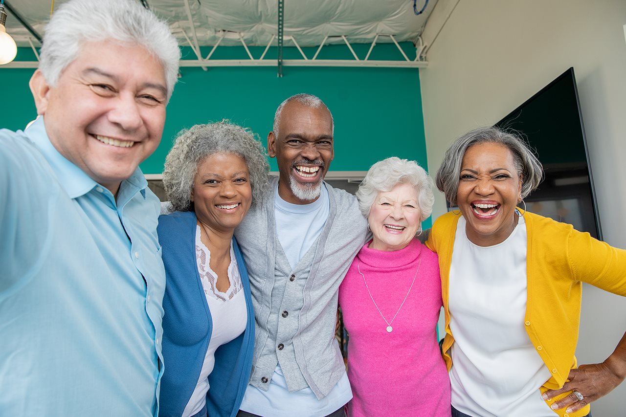A group of laughing seniors taking a selfie in the community room.