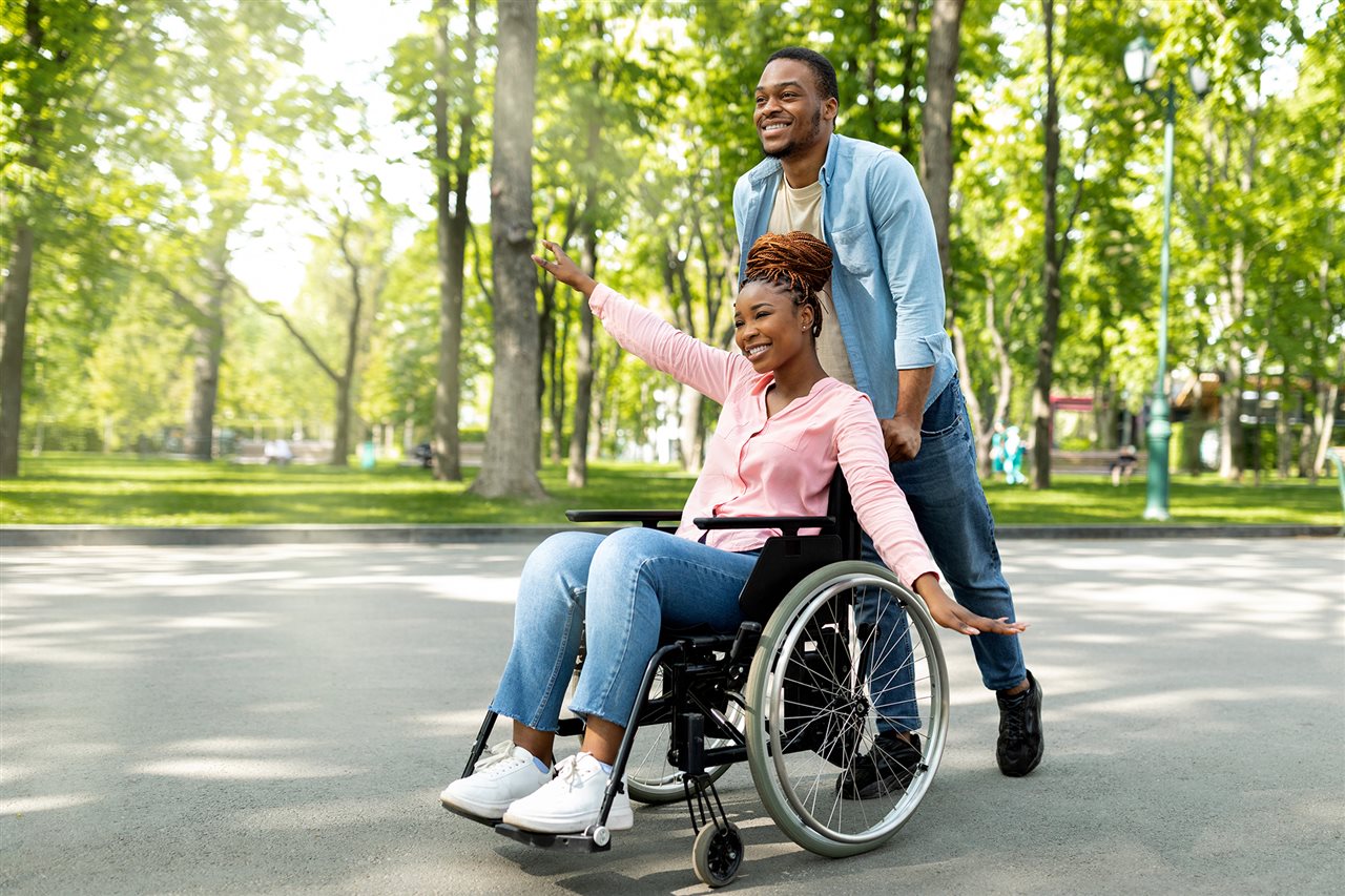 Hombre empujando a una mujer en una silla de ruedas en un parque. Una persona puede ser elegible para un Periodo de Inscripci&oacute;n Especial si experimenta eventos de vida calificados.