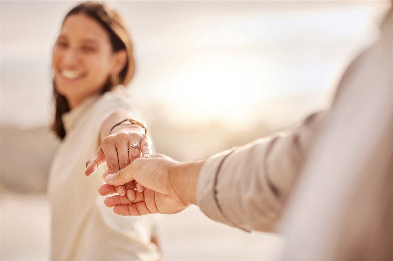 A couple in soft focus holds hands, revealing an engagement ring.