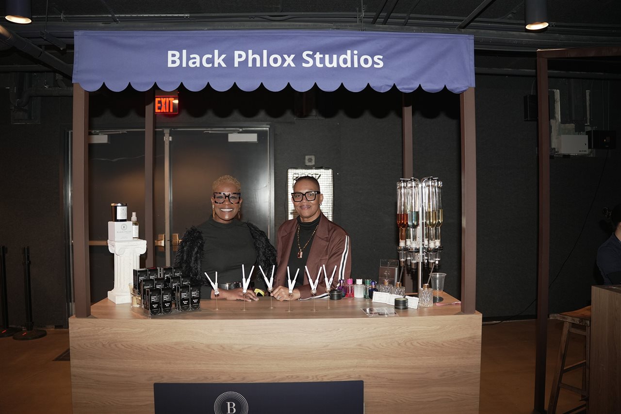 Two vendors at a kiosk selling scented items with a purple banner above reading