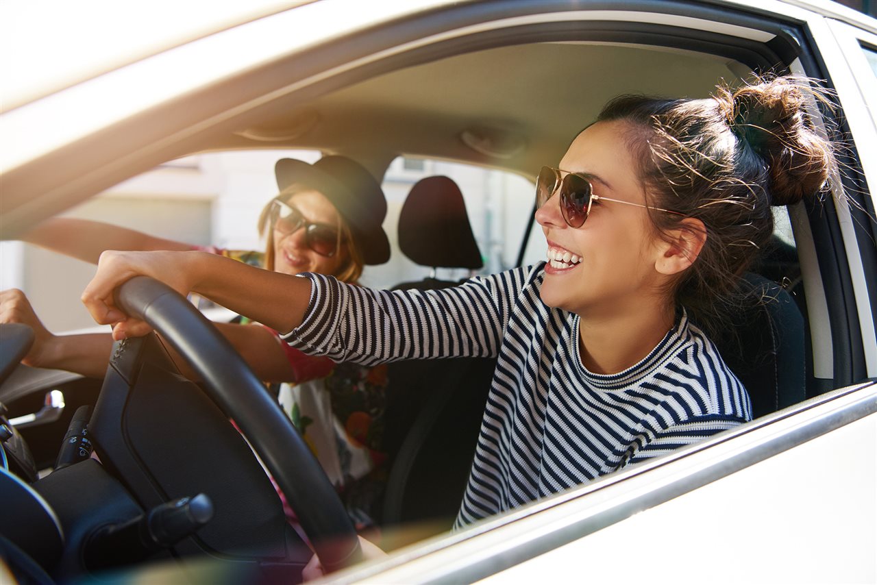 Two young women having fun driving a car. Flexcar provides car subscriptions services.