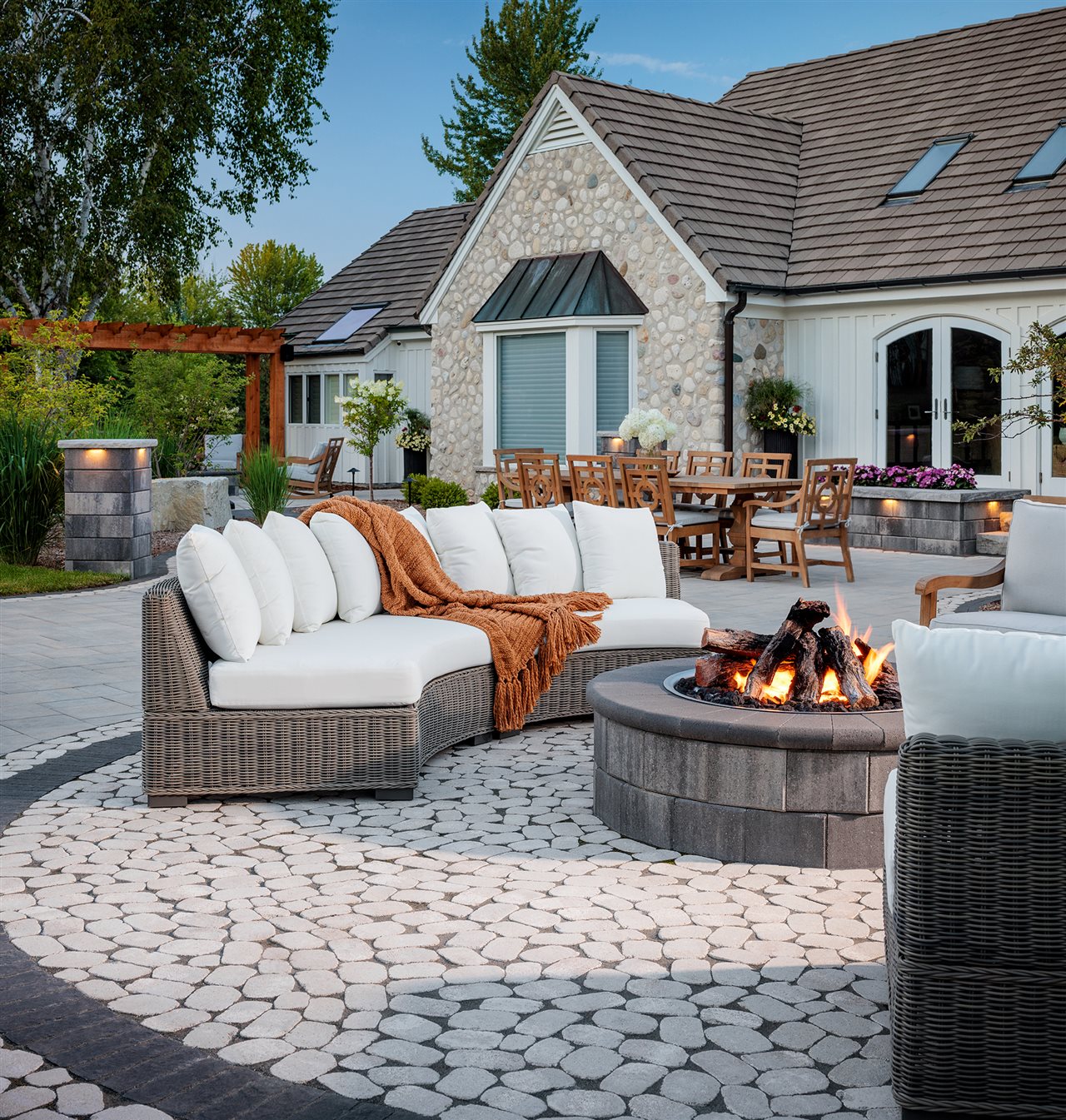 Upscale home with lovely outdoor paver patio featuring raised planters, pergala, dining area, cozy sectional wicker sofa and fire feature.