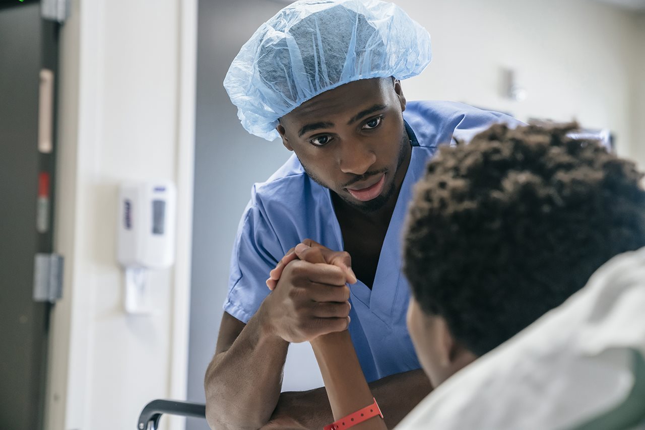 Male nurse consouling a patient in a hospital bed.