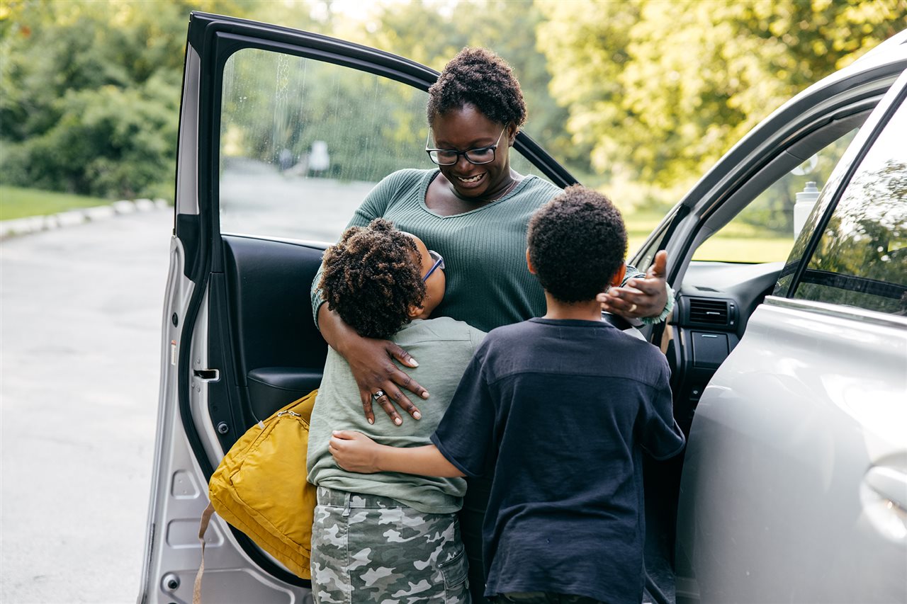 Mom getting out of her SUV and giving her two boys a hug before droping them off at school.