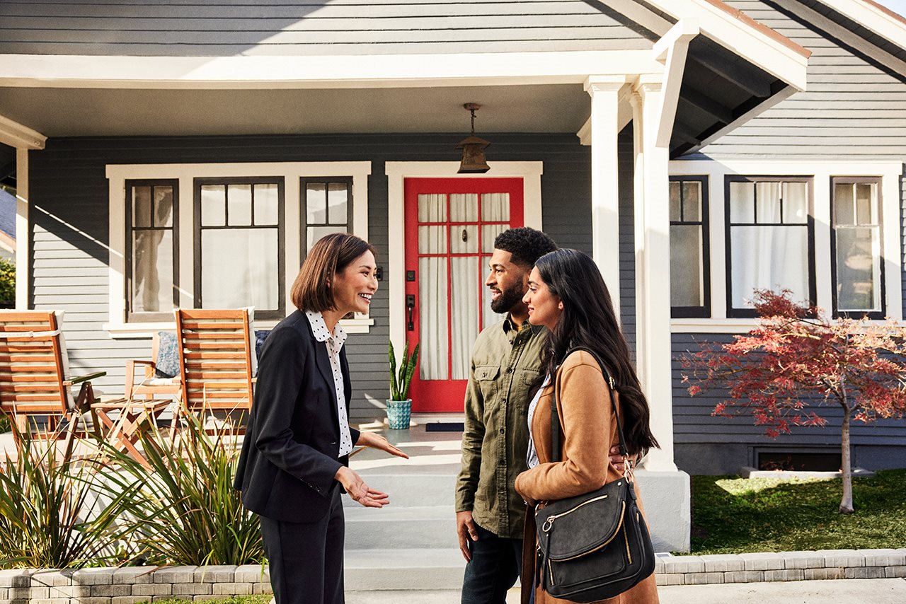 A couple speaks with a realtor in front of a prospective home.