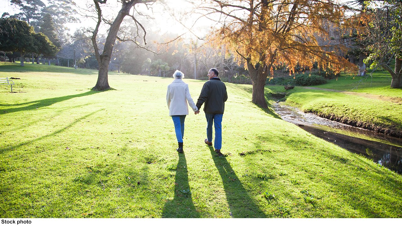 Man and woman walking across the grass in a park during the Fall.
