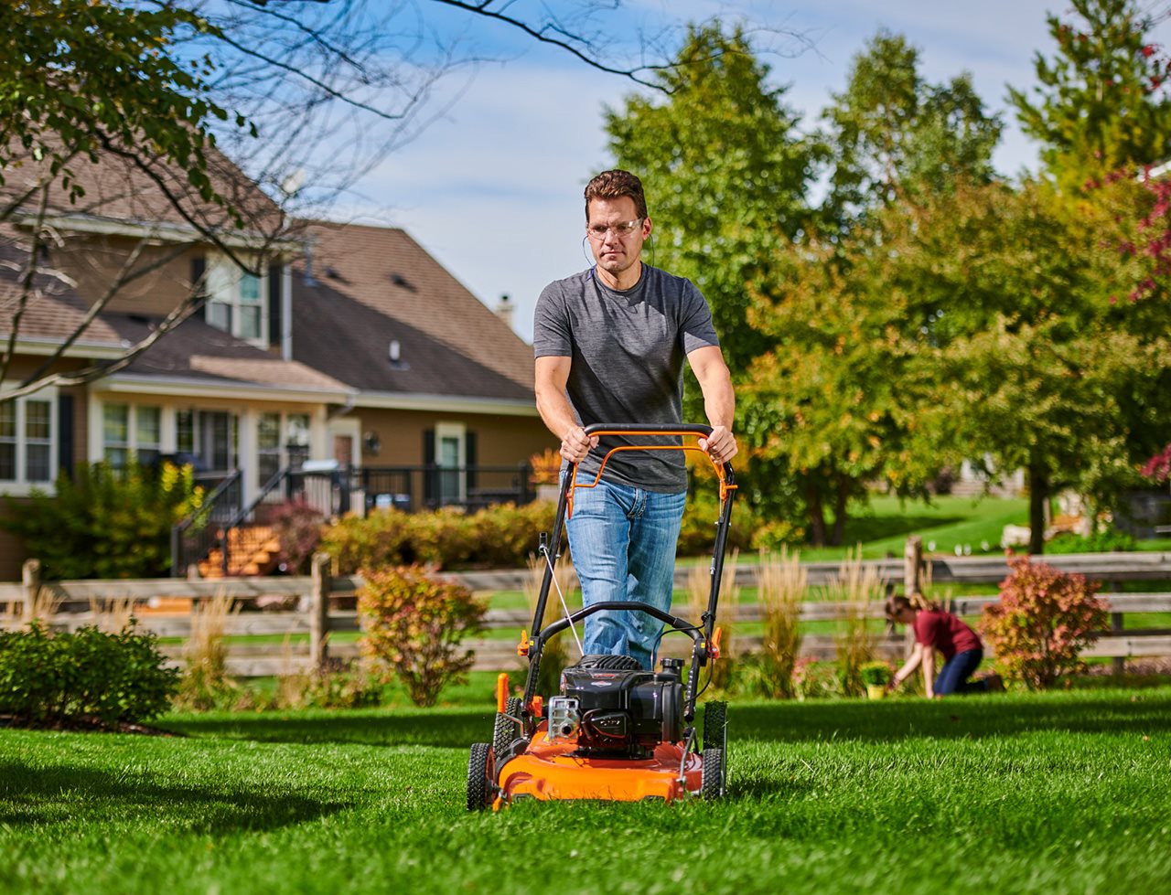 Man using a gas-powered mower to cut his lawn. Briggs and Stratton lawn mowers are durable and easy to use.