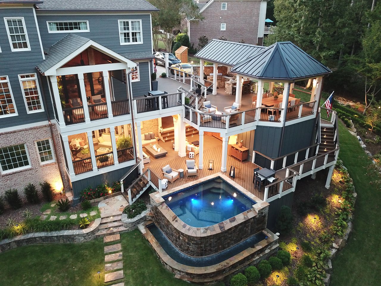 Massive double deck with upstairs outdoor kitchen, dining area under gazebo, and open seating area. Downstairs deck has seating area, pool area, and storage area.
