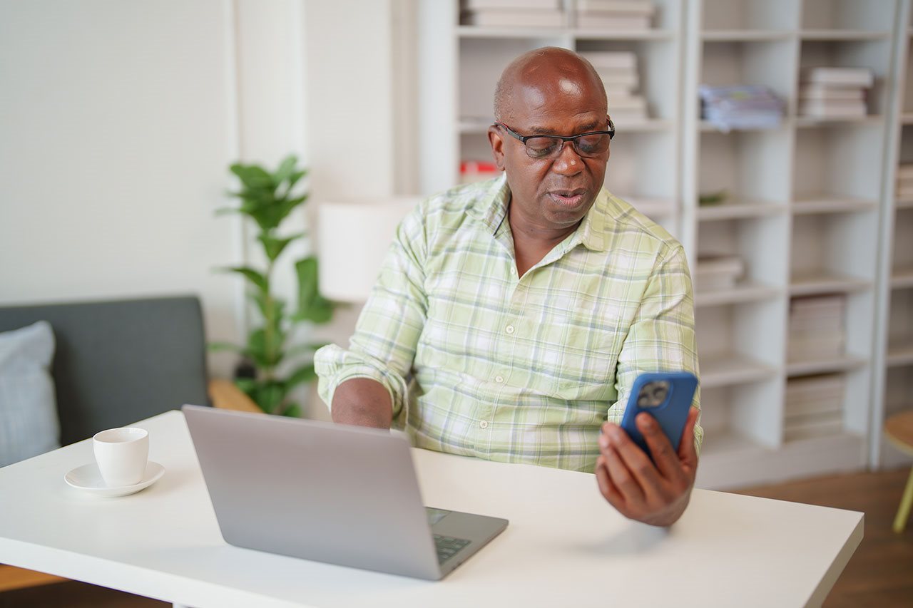 Senior man looking at and odd text on his phone while in his home office