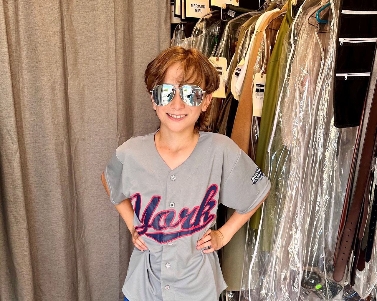 Christian, wearing sunglasses, stands with his hands on his hips in front of a wardrobe rack.